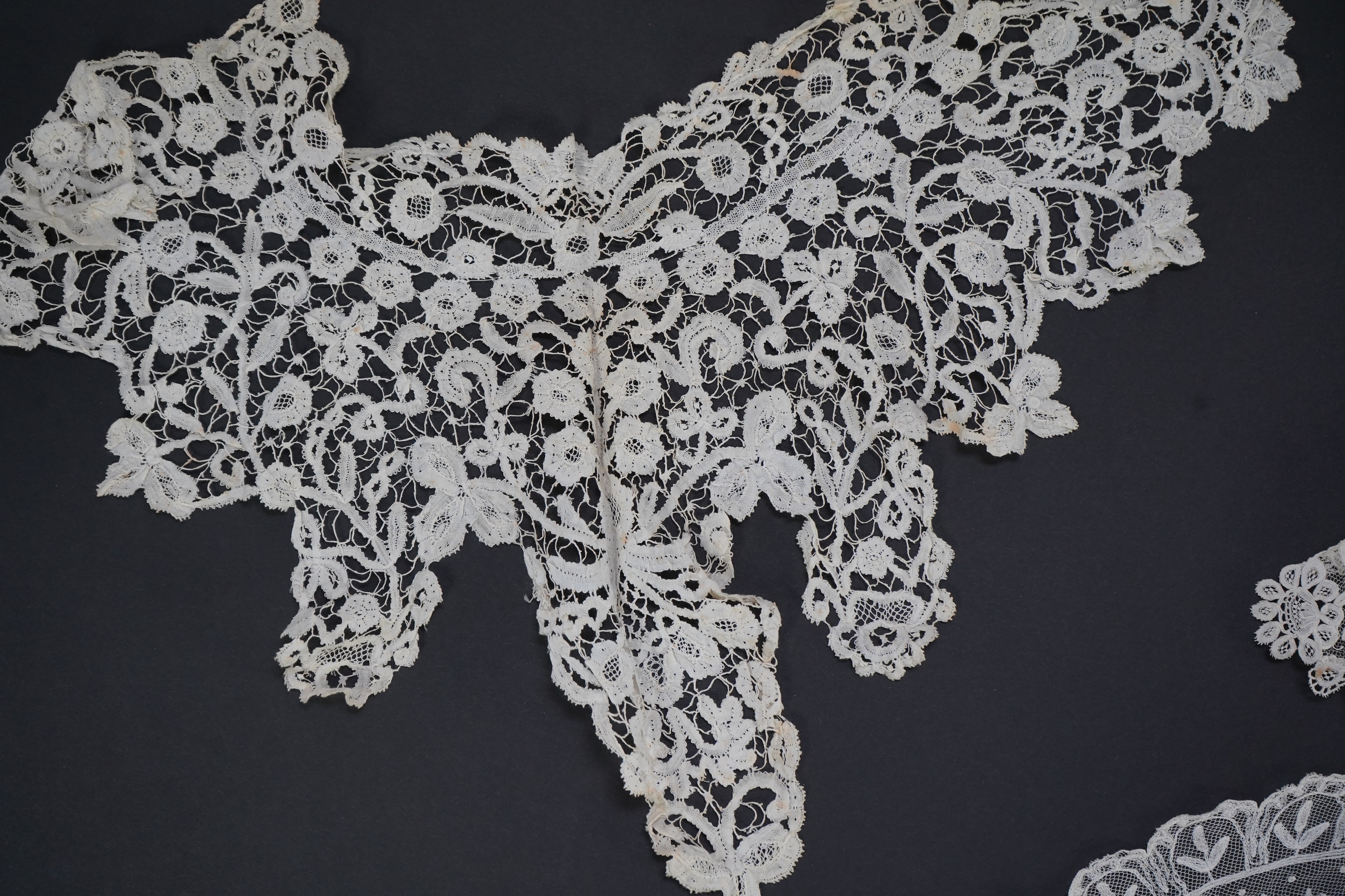 A white tape lace on net bed cover, a cream lace needle run panel, three Brussels bobbin lace collars, a lappet and two beaded tea pot covers, bed cover 200cm x 250cm. Condition - the bedcover has damage to the netting,